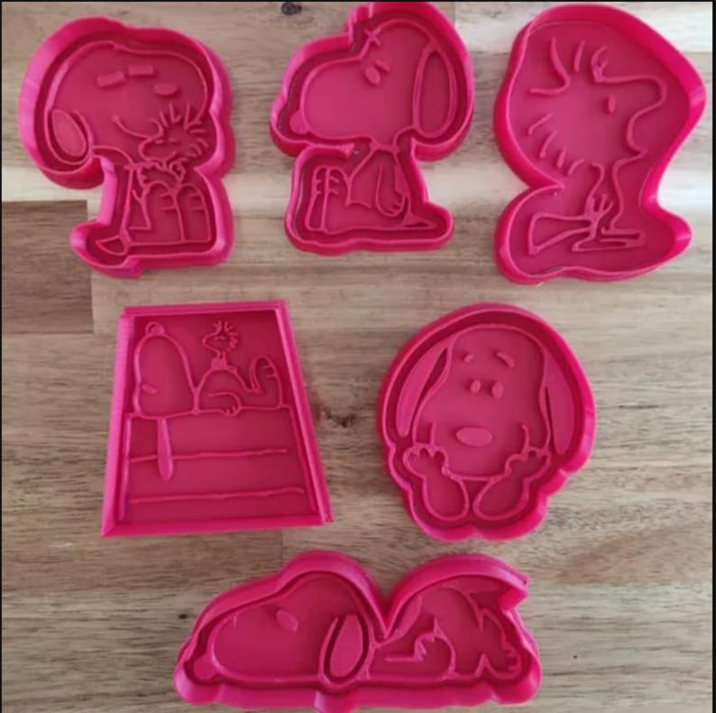 May include: Set of six red plastic cookie cutters featuring different poses of the cartoon character Snoopy.