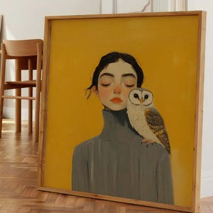 May include: A square framed painting featuring a portrait of a person with dark hair wearing a grey turtleneck sweater, with a barn owl perched on their shoulder. The background of the artwork is a solid, vibrant yellow color.