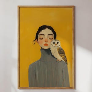 May include: A framed art print featuring a portrait of a person with dark hair and closed eyes, wearing a grey turtleneck jumper. A barn owl with white and brown feathers is perched on the person's shoulder against a solid yellow background.