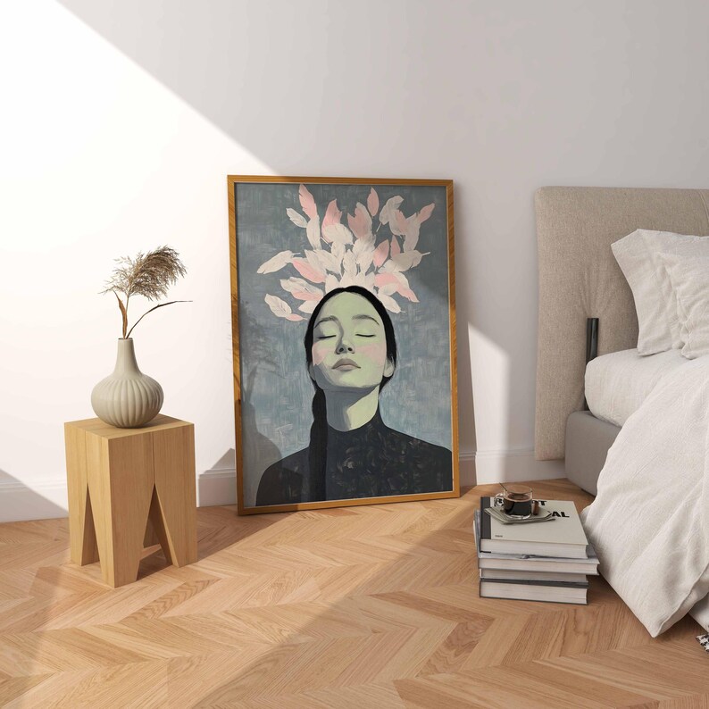 May include: A framed print of a woman with her eyes closed, surrounded by pink and white feathers. The woman is wearing a black mock neck shirt and has long dark hair. The background is a light blue color.