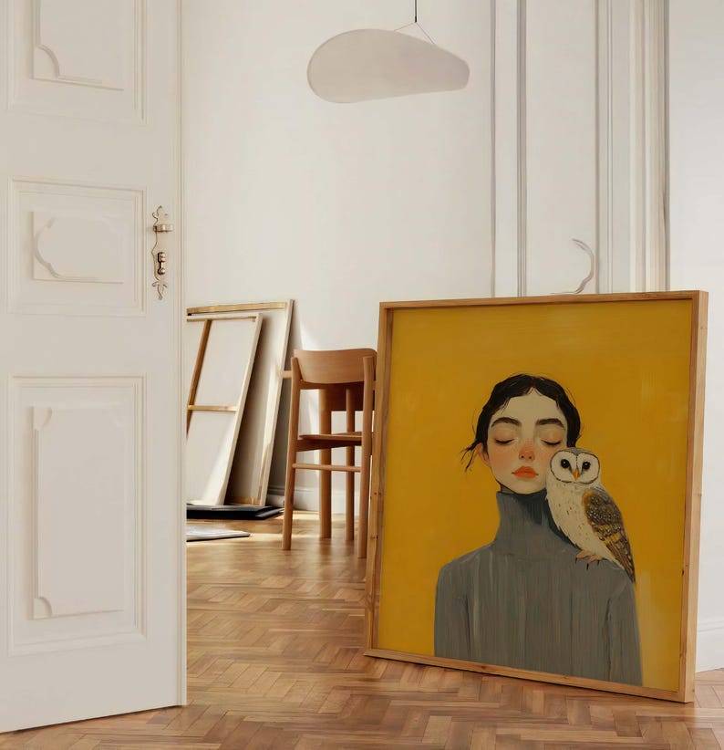 May include: A square framed painting featuring a portrait of a person with dark hair wearing a grey turtleneck sweater, with a barn owl perched on their shoulder. The background of the artwork is a solid, vibrant yellow color.