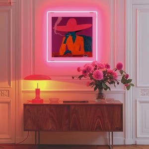 May include: A wooden cabinet with a red lamp on top and a vase of pink flowers. A neon sign with a woman wearing a red hat and smoking is hanging on the wall above the cabinet.