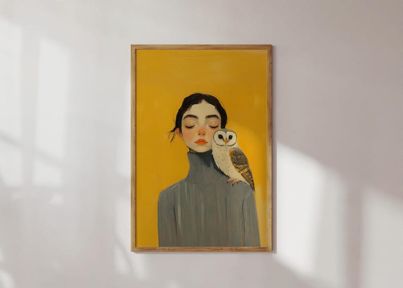 May include: A framed art print featuring a portrait of a person with dark hair and closed eyes, wearing a grey turtleneck jumper. A barn owl with white and brown feathers is perched on the person's shoulder against a solid yellow background.