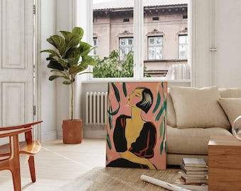 May include: An art print featuring a woman in a black dress with a yellow face and short black hair, set against a pink background with green brushstrokes. The artwork is displayed in a well-lit room with a plant and a wooden chair.