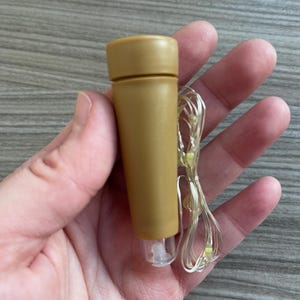 May include: A tan bottle stopper with a cylindrical design, featuring a small clear plastic base and a string of tiny LED lights. The stopper is designed to fit into a bottle opening. The lights are on a thin, flexible silver wire.
