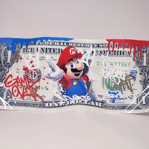 May include: A one dollar bill with a red, white and blue paint splatter design. The bill features a cartoon image of Mario from the Super Mario video game series. The text "GAME OVER" is written in red and white paint on the bill.