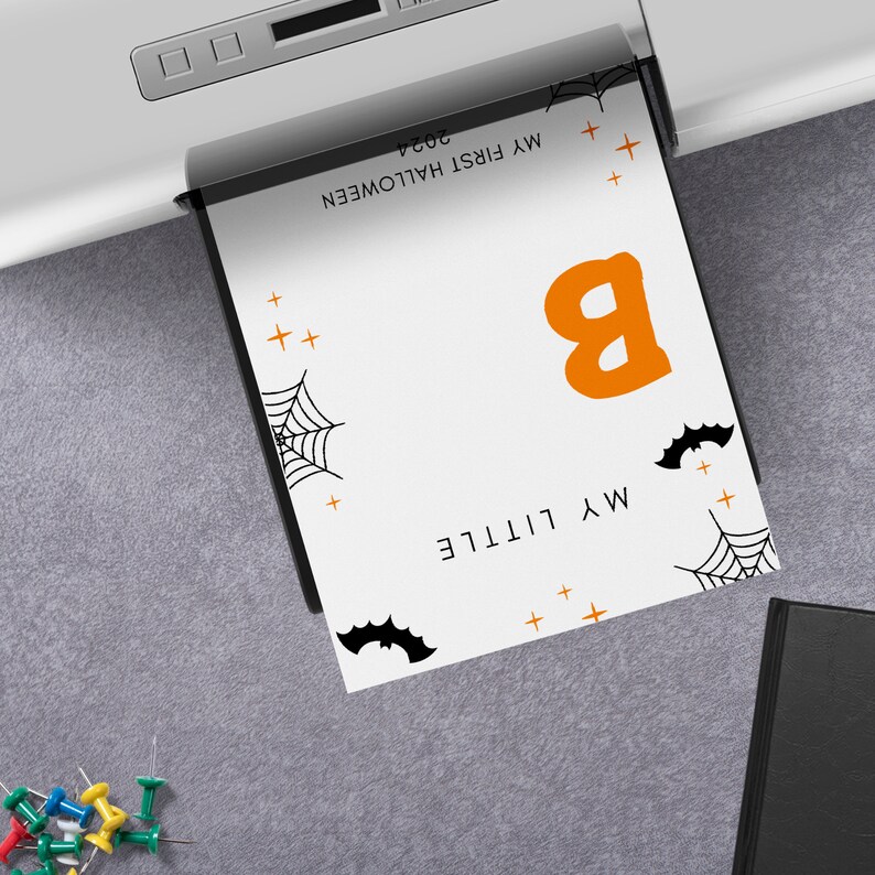 K&ouml;nnte beinhalten: Eine wei&szlig;e Karte mit schwarzen und orangefarbenen Halloween-Dekorationen. Die Karte sagt "My Little B" und "My First Halloween 2024".