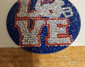 May include: A circular, blue decorative piece featuring the word "LOVE" in silver and red rhinestones. The surrounding area is also adorned with blue rhinestones. This item could be a decorative accessory or embellishment.