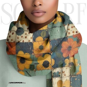 Puede incluir: Bufanda estampada con un diseño floral en tonos amarillos, naranjas, azules y verdes. La bufanda tiene un diseño de patchwork con un aspecto envejecido y vintage. La palabra "SCARF" está impresa en letras blancas grandes en la parte superior.