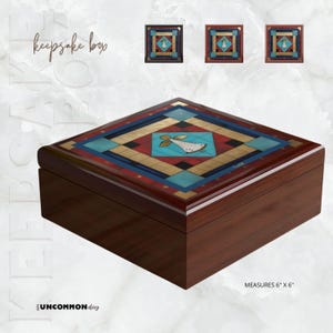 Op de afbeelding: Vierkante bewaardoos met een donkere houten afwerking. Het deksel heeft een geometrisch ontwerp met turquoise, rode, gouden en zwarte accenten en een centrale engelillustratie. Afmetingen: 15 cm x 15 cm.