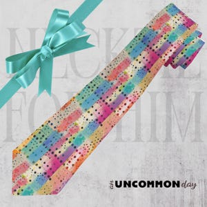 Op de afbeelding: Een kleurrijke stropdas met een aquarelontwerp met verticale strepen in roze, blauw, groen en geel, geaccentueerd met zwarte stippen. De stropdas wordt gepresenteerd met een turquoise lint. De tekst luidt "NICKED FOR HIM" en "an UNCOMMON day".