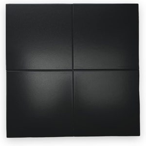May include: A black square tile with a smooth, glossy finish. The tile is divided into four equal squares by thin lines.