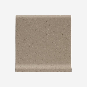 May include: A section of tan-colored baseboard molding with a speckled texture. The molding has a rounded top edge and a curved bottom edge, designed to sit flush against a wall and floor.