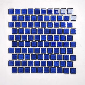 May include: A sheet of small, square, blue ceramic tiles with black grout lines. The tiles have a slightly textured surface.