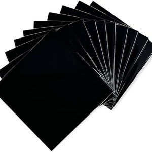 May include: A stack of ten black square tiles. The tiles are arranged in a fan shape, with the top tile being the largest and the bottom tile being the smallest.