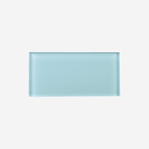 May include: A rectangular, light blue glass tile. The tile has a smooth, frosted appearance and is set against a white background. The edges are slightly rounded, giving it a soft look. This tile is suitable for various home decor projects.
