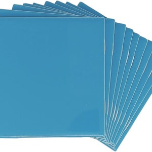 May include: A stack of ten light blue square tiles. The tiles are smooth and glossy.