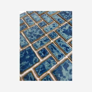 May include: Close-up of a mosaic tile sheet featuring rectangular and square tiles in shades of blue. The tiles have a textured, mottled appearance with a glossy finish. The grout lines are a light beige color.