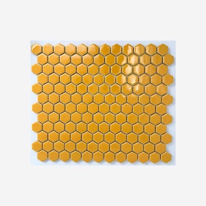 May include: A square of honeycomb-shaped, glossy, yellow tiles. The tiles are arranged in a grid pattern, creating a visually appealing surface. The tiles are a warm, golden yellow color, and the surface is smooth and reflective.