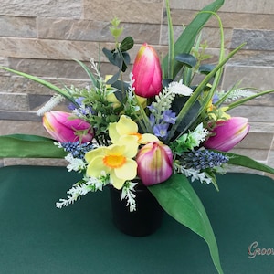 May include: A floral arrangement in a black vase with pink and yellow tulips, white and blue flowers, and green leaves.