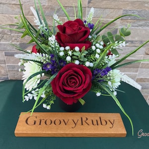 May include: A red rose bouquet with white and purple flowers in a black vase. The bouquet is sitting on a wooden sign that says "Groovy Ruby".