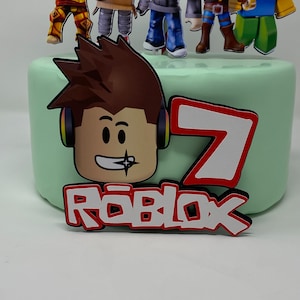 Może przedstawiać: Zielony tort z czerwono-białym logo Roblox, czerwoną cyfrą 7 i kresk&oacute;wkową postacią Roblox z brązowymi włosami i słuchawkami.