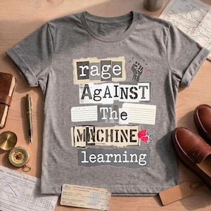 Puede incluir: Una camiseta gris jaspeado de manga corta con un gráfico estilo collage que incluye el texto "rage AgAiNST The MACHINE learning". El diseño presenta un icono de puño negro, detalles de rayos rojos y una pequeña ilustración de un cerebro.