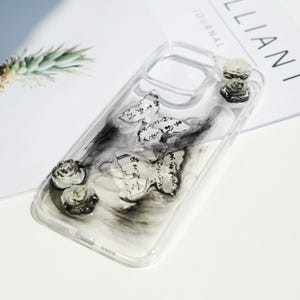 May include: Transparent phone case with butterfly and rose decorations. The case has two butterfly adornments with script and three small rose accents. The background has a black and white marbled effect.