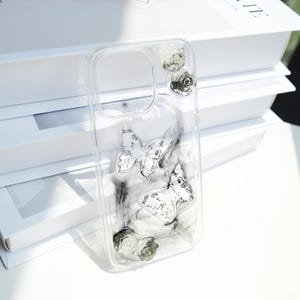 May include: Transparent phone case decorated with butterfly and rose motifs. The case showcases two butterfly designs with detailed patterns and three small rose accents. The butterflies and roses are in shades of white and grey.