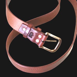 Peut inclure: Une ceinture en cuir marron avec une boucle en laiton. La ceinture est de couleur marron moyen et poss&egrave;de une boucle rectangulaire. La ceinture est incurv&eacute;e et semble neuve.