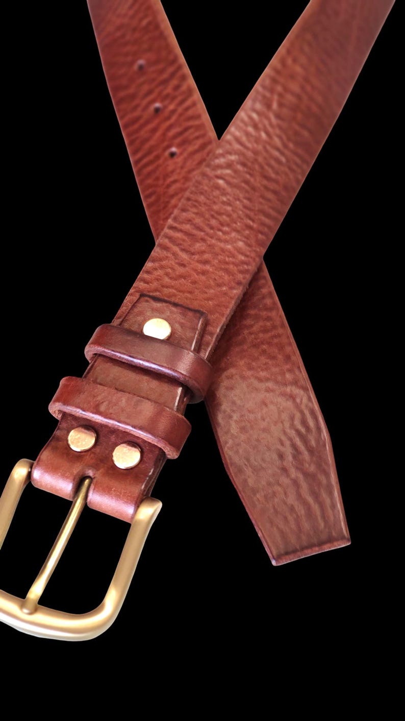 Peut inclure: Une ceinture en cuir marron avec une boucle dor&eacute;e. La ceinture a une surface textur&eacute;e et est fix&eacute;e avec des rivets de couleur laiton. La boucle est rectangulaire et la ceinture est pr&eacute;sent&eacute;e sur fond noir.