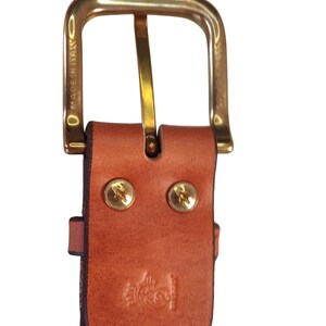 Puede incluir: Primer plano de un cintur&oacute;n de cuero marr&oacute;n con una hebilla dorada. El cintur&oacute;n tiene remaches dorados y un dise&ntilde;o en relieve decorativo. Las palabras "MADE IN ITALY" son visibles en la hebilla.