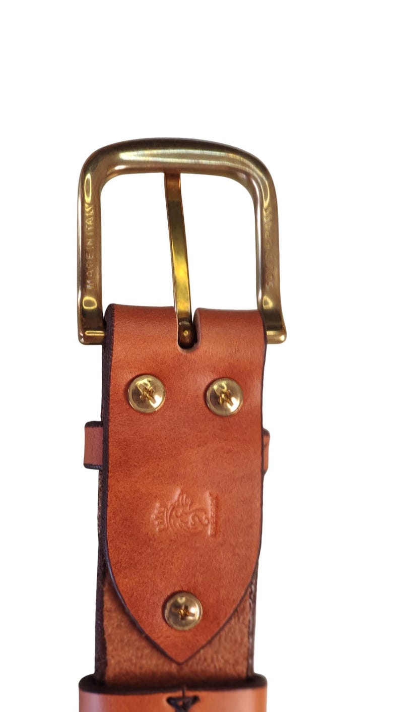 Puede incluir: Primer plano de un cintur&oacute;n de cuero marr&oacute;n con una hebilla dorada. El cintur&oacute;n tiene remaches dorados y un dise&ntilde;o en relieve decorativo. Las palabras "MADE IN ITALY" son visibles en la hebilla.