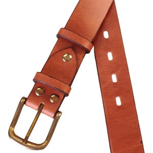 Puede incluir: Un cintur&oacute;n de cuero marr&oacute;n claro con hebilla y remaches de lat&oacute;n. El cintur&oacute;n tiene un dise&ntilde;o cl&aacute;sico con una hebilla rectangular y m&uacute;ltiples agujeros para ajustar. El cuero parece ser de alta calidad, con una textura suave y un color c&aacute;lido y natural.
