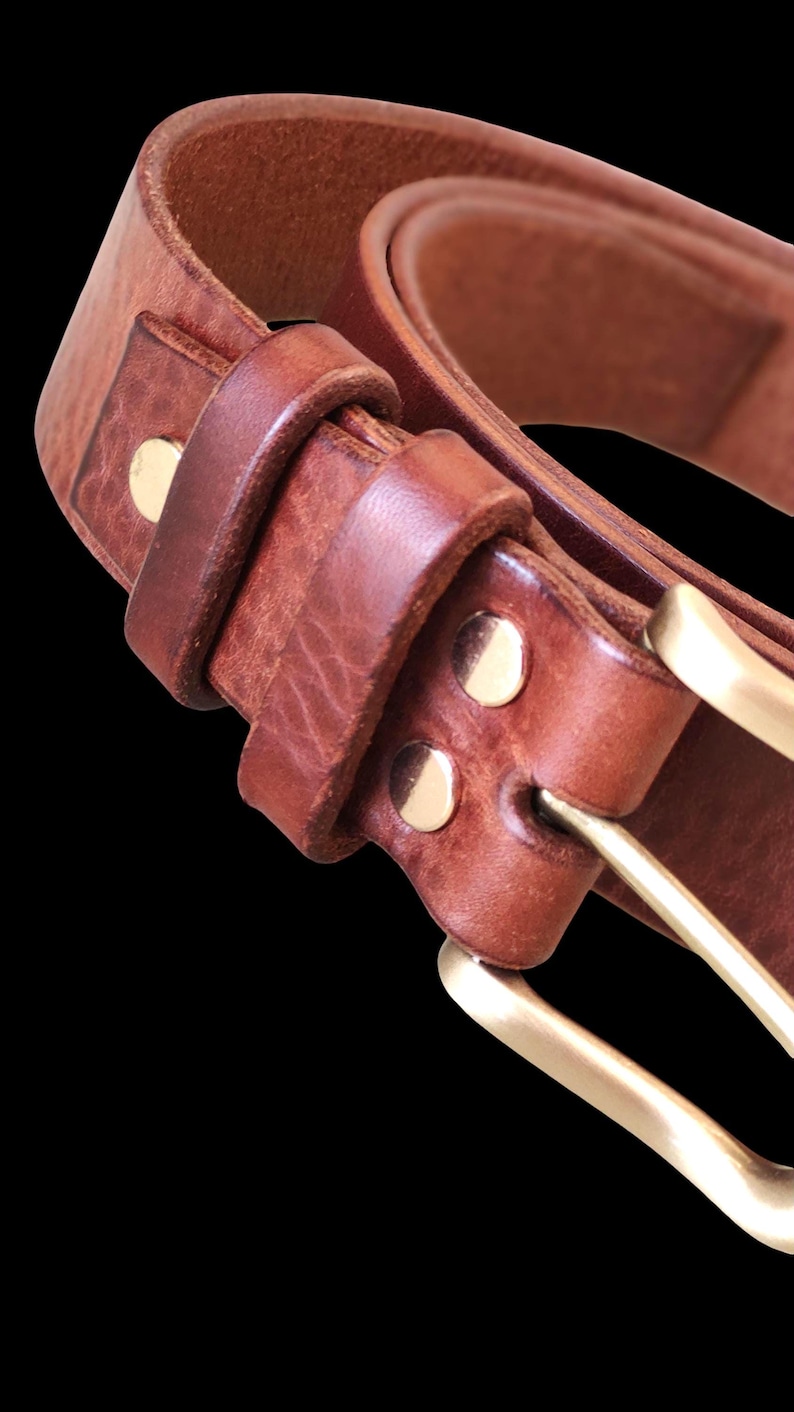 Peut inclure: Gros plan sur une ceinture en cuir marron avec une boucle et des rivets en laiton. La ceinture est faite d'un cuir &eacute;pais et textur&eacute; et a un design classique. La boucle en laiton ajoute une touche d'&eacute;l&eacute;gance.
