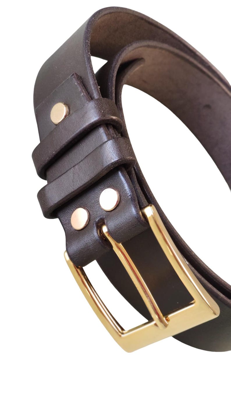 K&ouml;nnte beinhalten: Nahaufnahme eines braunen Lederg&uuml;rtels mit goldfarbener Schnalle. Der G&uuml;rtel hat zwei goldene Nieten in der N&auml;he der Schnalle und eine Schlaufe, um den G&uuml;rtel an Ort und Stelle zu halten. Der G&uuml;rtel ist gebogen und scheint neu zu sein.
