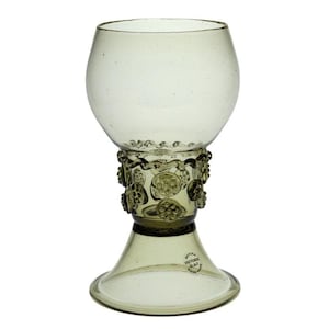 May include: A green glass goblet with a decorative, textured base. The base has a circular design with a raised, embossed pattern. The goblet is clear and has a round, wide bowl.