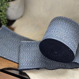 May include: A roll of blue and white herringbone patterned fabric, partially unrolled, displaying a chevron design. The fabric has a dark blue core and is displayed on a light-coloured surface.