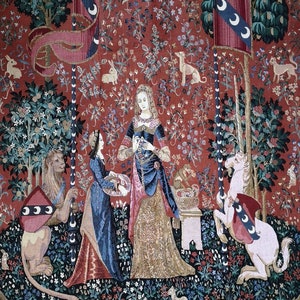 May include: A tapestry depicting a scene from the Unicorn Tapestries. A woman in a gold and blue gown stands with a unicorn and a lion. The unicorn is white and has a red and blue flag with crescent moons. The lion is brown and has a red and blue flag with crescent moons. The woman is holding a flower in her hand. The tapestry is set against a red background with a variety of flowers and plants.