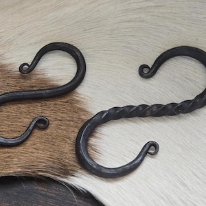 Könnte beinhalten: Zwei schwarze Metallhaken, einer mit einem gedrehten Design und der andere mit einer glatten Oberfläche. Beide Haken haben eine abgerundete Form und sind ideal zum Aufhängen von Gegenständen.