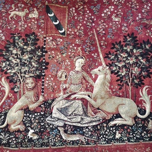 May include: A tapestry depicting a unicorn being led by a woman to a pool of water. The unicorn is white with a gold horn and the woman is wearing a blue dress. The tapestry is surrounded by a red background with green trees and flowers.