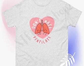 May include: A gray t-shirt with a pink heart design. The heart has a pair of cartoon lungs inside with the text "Don't Hate Ventilate" around the heart.
