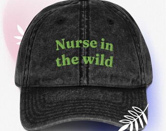 May include: A black, distressed baseball cap with the embroidered text "Nurse in the wild" in green. The cap has a curved brim and a classic six-panel design. A stylish accessory for healthcare professionals.