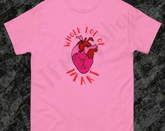 May include: Pink t-shirt with a graphic of a heart in shades of pink and red. The words "WHOLE LOT OF HEART" are written around the heart in red. The shirt is made of a soft material and has short sleeves.