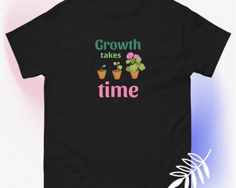 May include: Black t-shirt with the text "Growth takes time" in green and pink. The design features three potted plants, illustrating the growth process. The first pot has a small sprout, the second has a growing plant, and the third has a flowering plant.