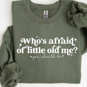 May include: A green sweatshirt with the text "Who's afraid of little old me? You should be" in white.