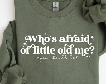 May include: A green sweatshirt with the text "Who's afraid of little old me? You should be" in white.