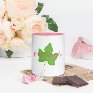 Puede incluir: Taza de cerámica blanca con borde rosa. La taza tiene un diseño de hoja verde y el texto "M-P Made" en letras rosas.