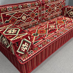 Op de afbeelding: Een rood en crèmekleurig vloerkleed met een geometrisch ontwerp. Het kussen is gemaakt van stof en heeft een gestoffeerde oppervlak. Het is een traditioneel kussen dat perfect is om op de vloer te zitten.