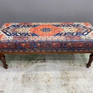 May include: A wooden bench with a colourful patterned cushion. The cushion features a geometric design in shades of red, orange, blue, and white.